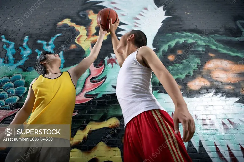 Teenage Boys Playing Basketball Next To Spray Painted Mural