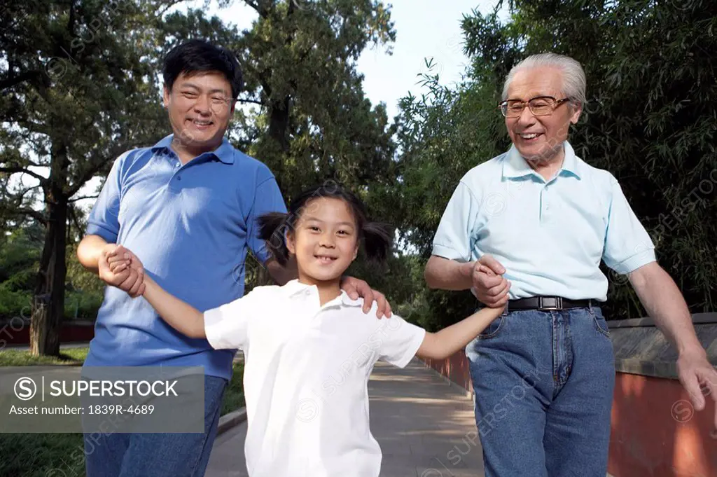 Little Girl Walking With Father And Grandfather Through The Park