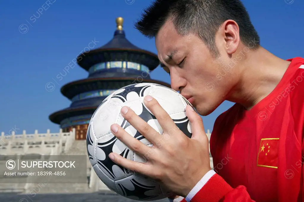 Young Male Soccer Player Kissing Soccer Ball In Front Of Temple