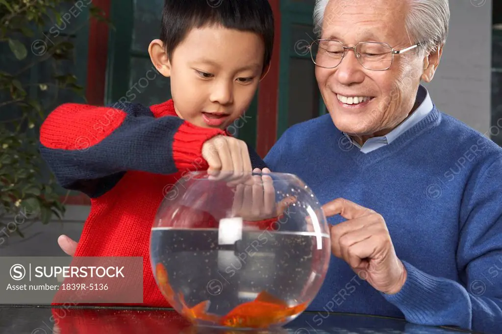 Elderly Man Showing Young Boy Goldfish In A Bowl