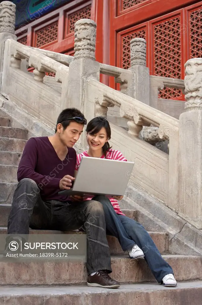 Young Couple Sitting On Stairs, Using Laptop