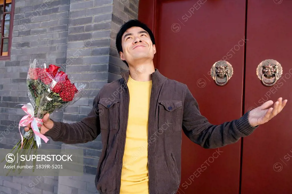 Young Man Waiting Outside Building Entrance Holding A Bunch Of Roses