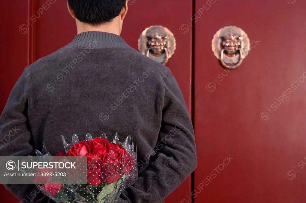 Young Man Waiting At Front Door With A Bunch Of Roses Behind His Back