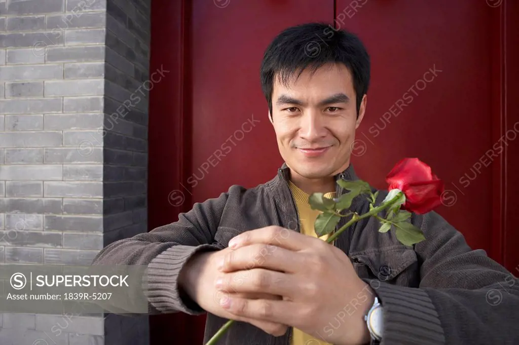 Young Man Waiting Outside Front Door Holding A Single Rose