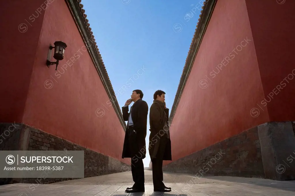 Businessmen Standing Back To Back Next To Building