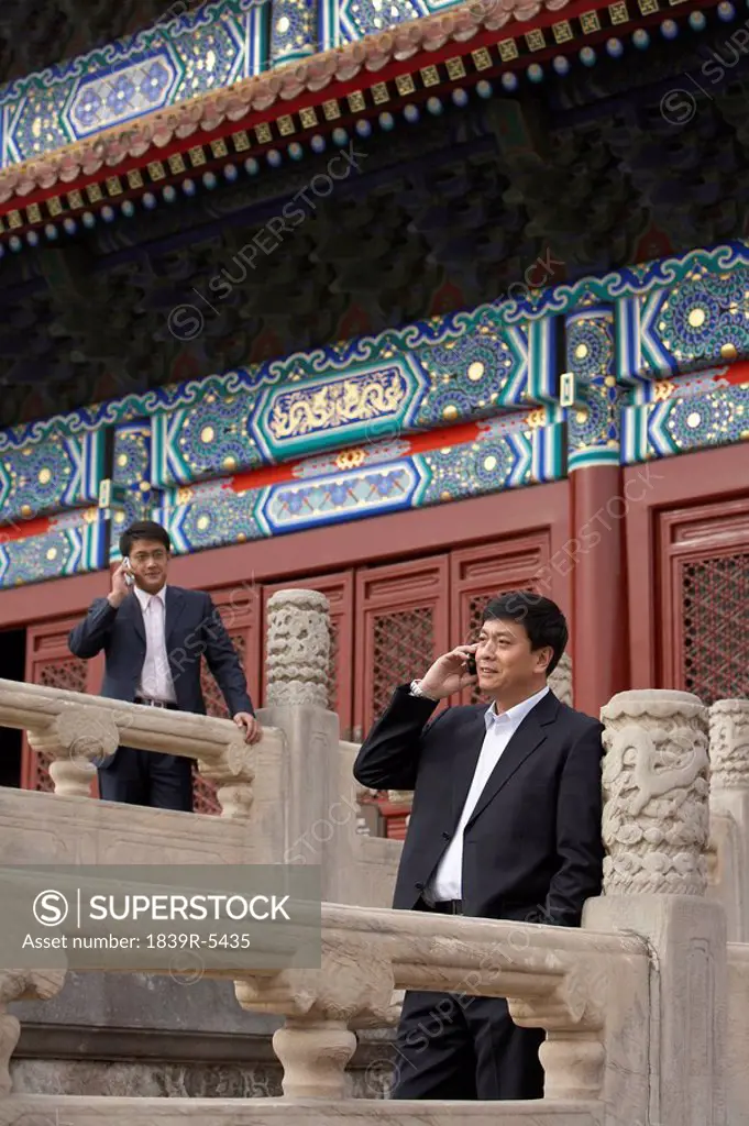 Two Businessmen Talking On Cellphones In The Forbidden City In Beijing