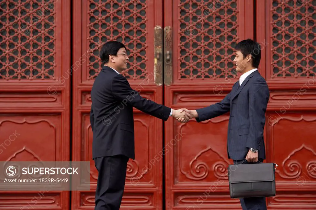 Two Businessmen Shaking Hands In Doorway Of The Forbidden City In Beijing