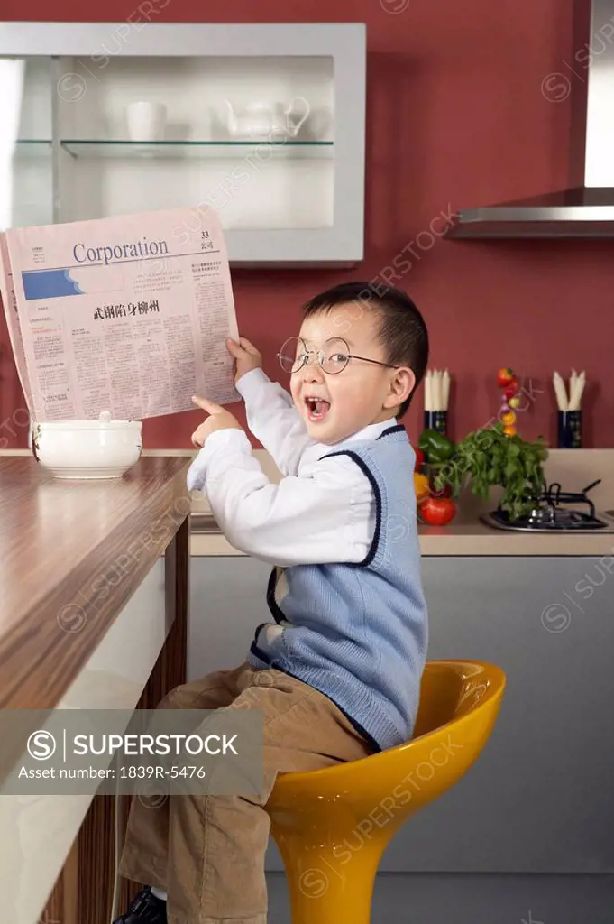 Young boy reading a business newspaper at the breakfast table