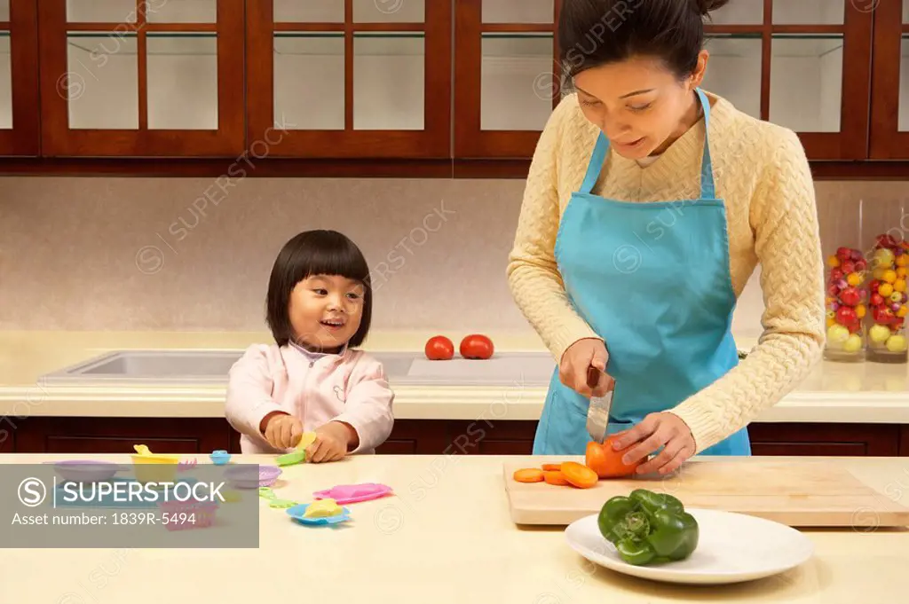 Young girl playing in the kitchen while her mother cooks