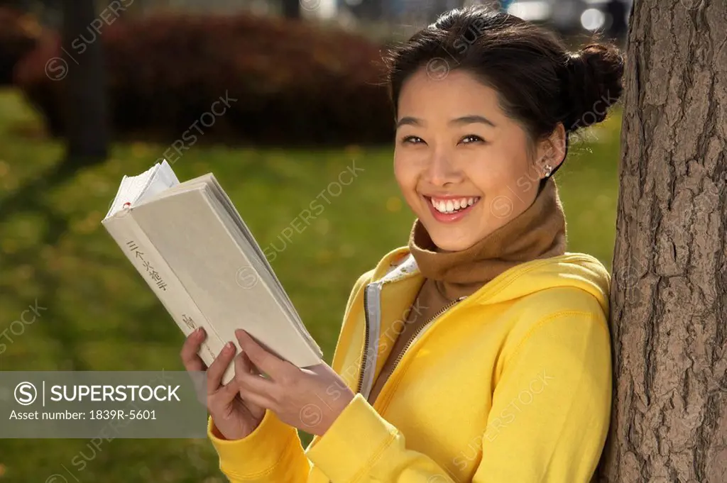 Young Woman Leaning Against A Tree Reading Her Book