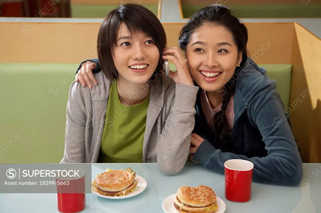 Teenage Girls Eating Burgers And Talking On Phone
