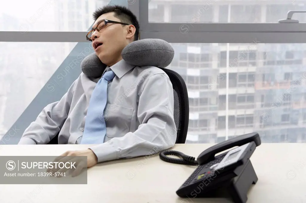 Businessman In Office Resting With Neck Pillow