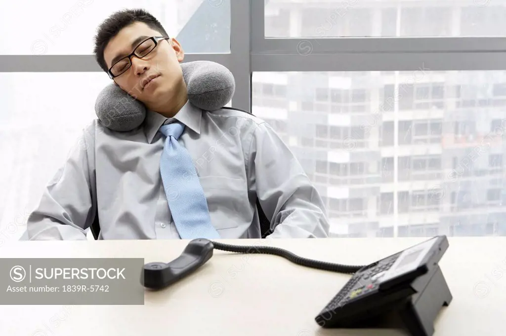 Businessman In Office Resting With Neck Pillow And Phone Off Hook