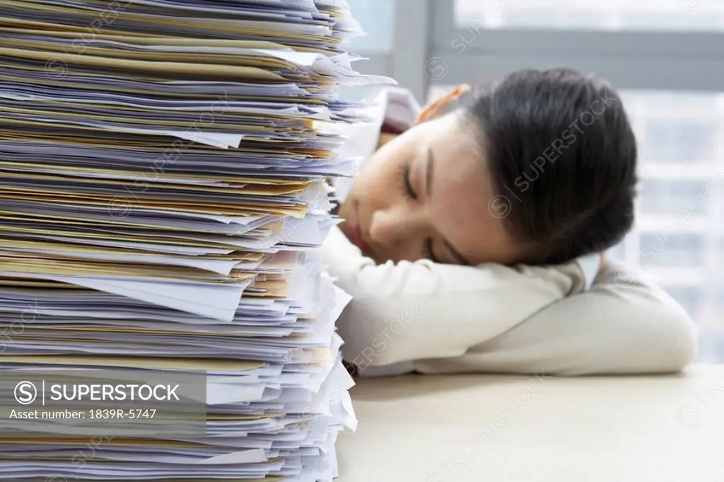 Businesswoman Sleeping Next To Pile Of Work