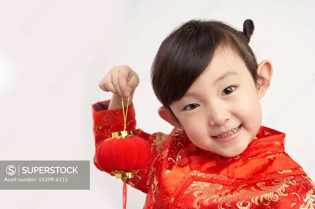 Young girl in festival Chinese New Year clothing, smiling at camera, holding Chinese lantern