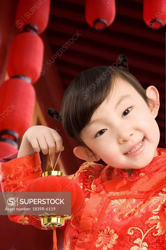 Young girl in festival Chinese New Year clothing, smiling at camera, holding Chinese lantern