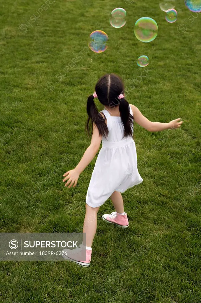 Young Girl Chasing Bubbles In Park