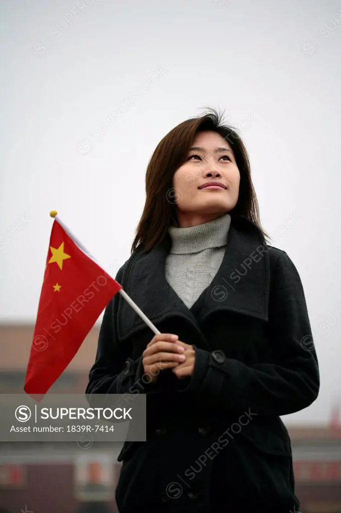 Young woman holding Chinese flag while visiting Tiananmen Square, Beijing, China