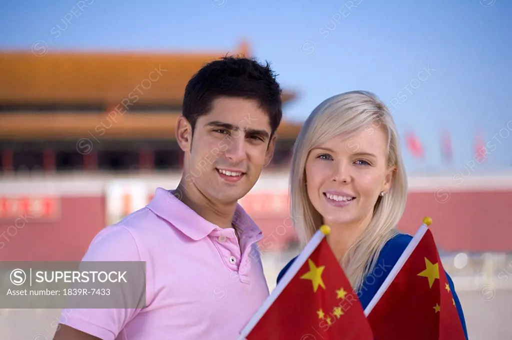 Young couple holding flags in front of Tiananmen Gate, Beijing, China