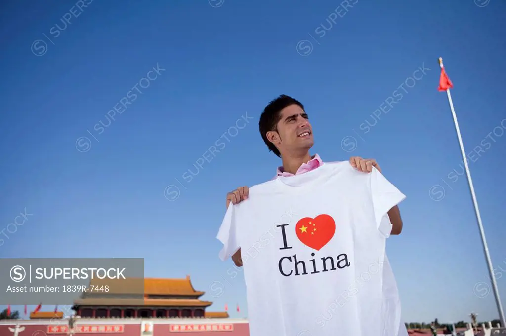 Young man holds an I Heart China t_shirt in front of Tiananmen Gate, Beijing, China