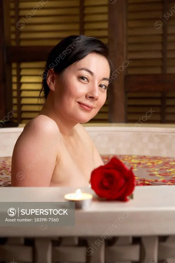 Woman relaxing in a rose petal bath with a rose and candle