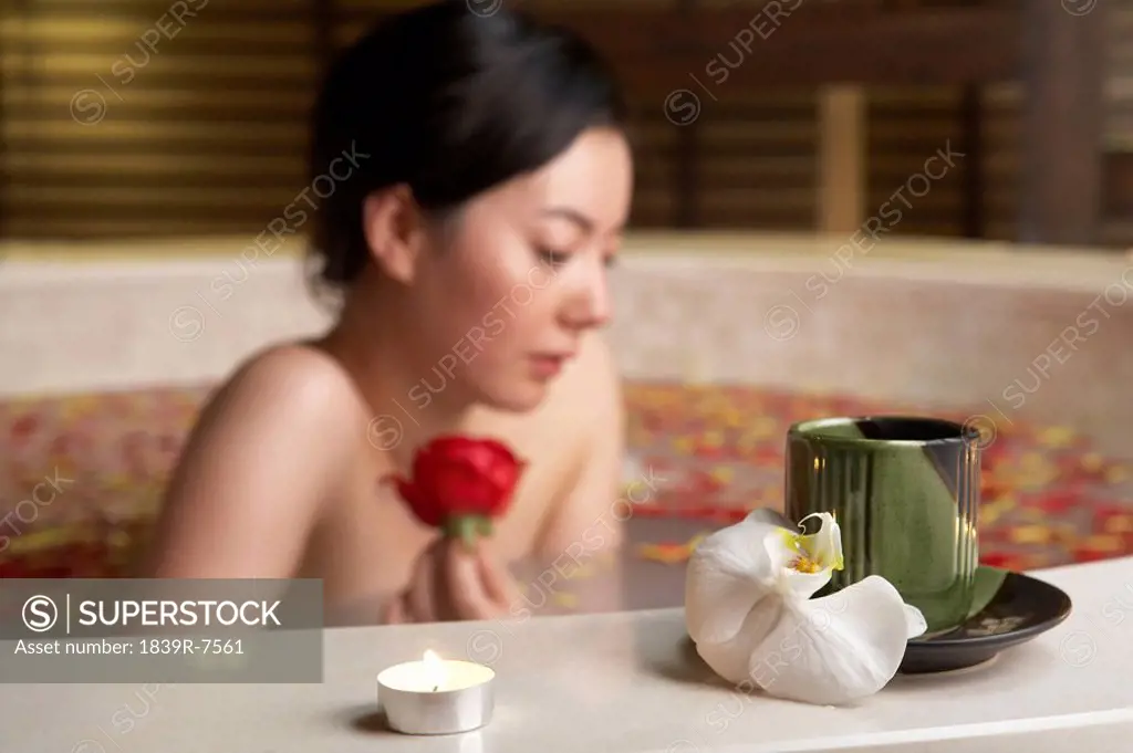 Woman relaxing in a rose petal bath with a rose and candle