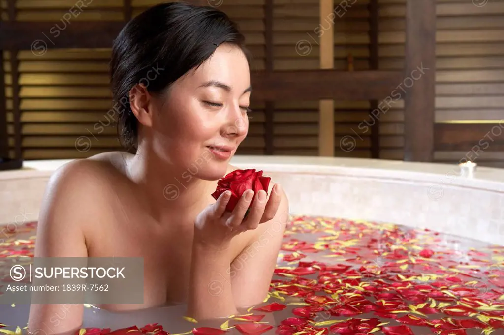 Woman relaxing in a rose petal bath with an orchid and candle
