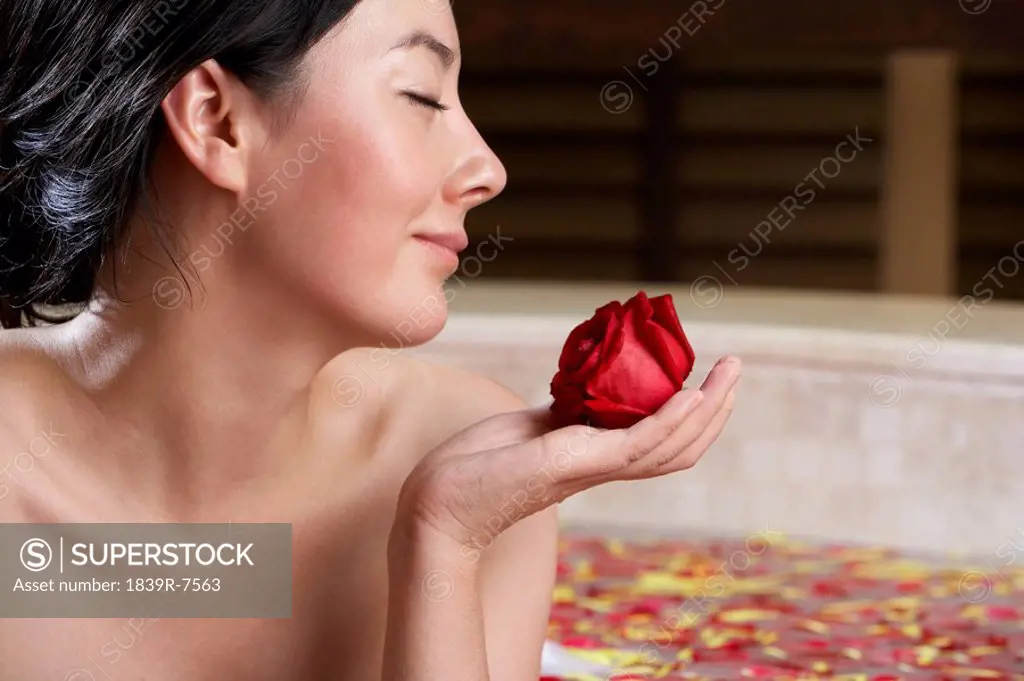 Woman relaxing in a rose petal bath with a rose