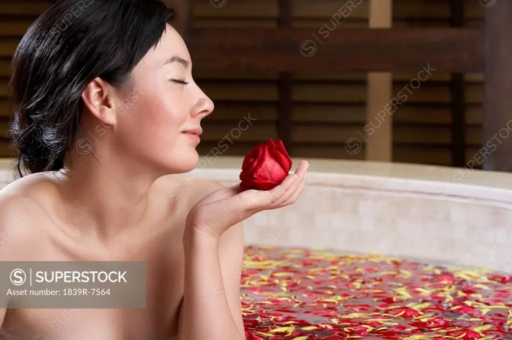 Woman relaxing in a rose petal bath with a rose