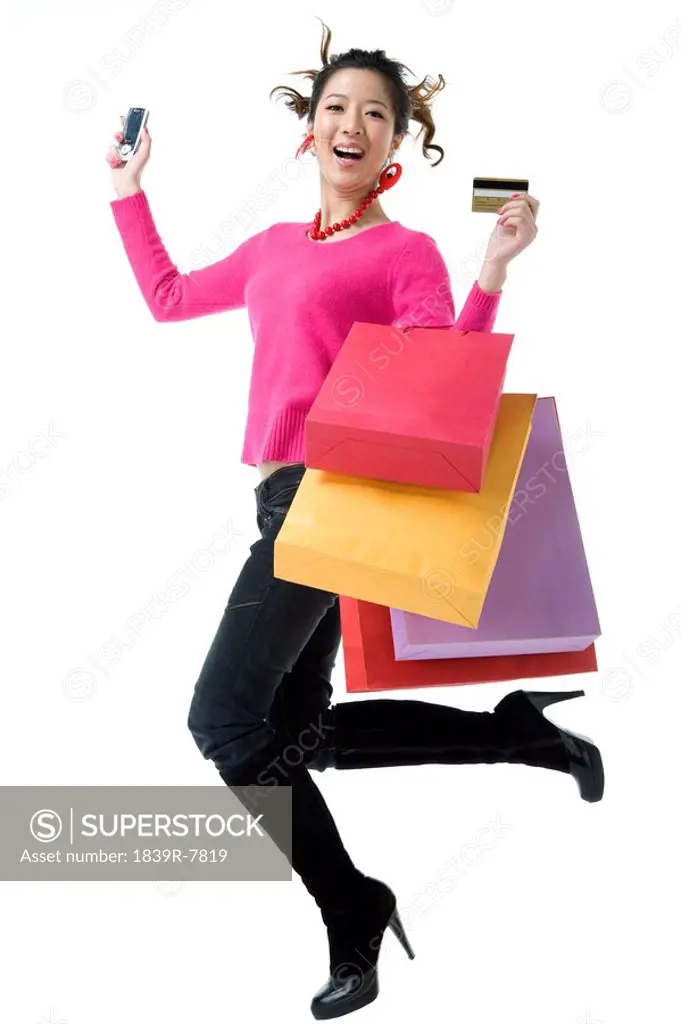 Young woman with shopping bags, credit card and mobile phone leaping
