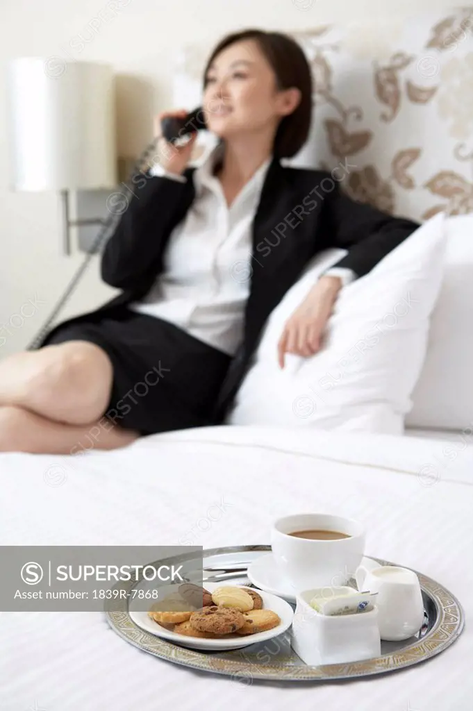 Shot of cookies and coffee in front of a woman in business attire talking on the telephone