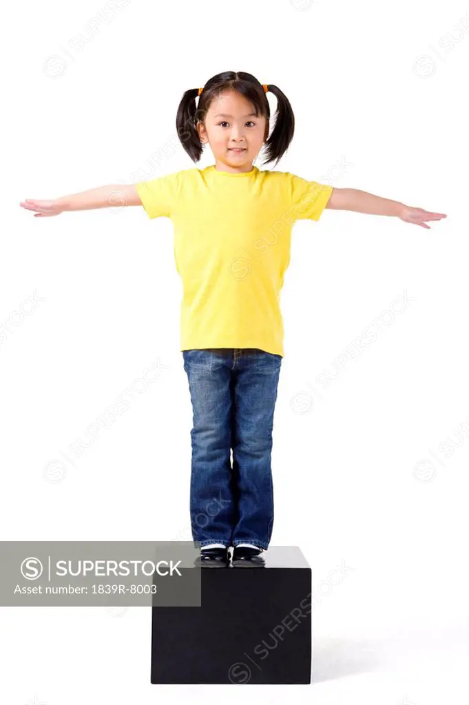 Little girl stands on some blocks with her arms streched out