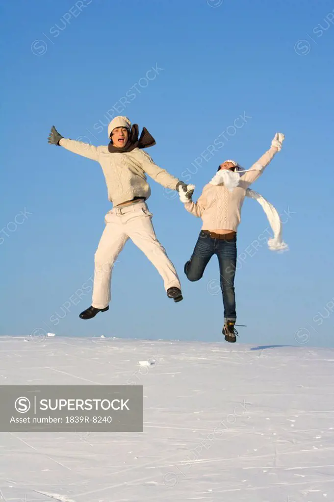 Young man and young woman jumping over a snowy landscape