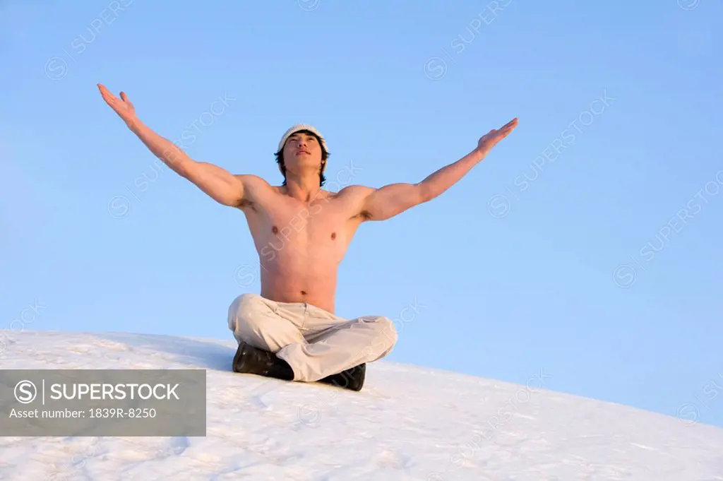 Young man raising his arms while sitting in snow