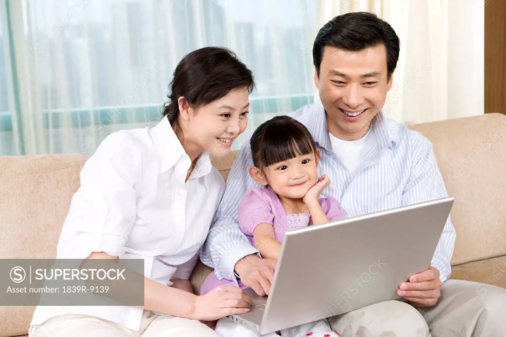 Young couple and daughter look at laptop on sofa