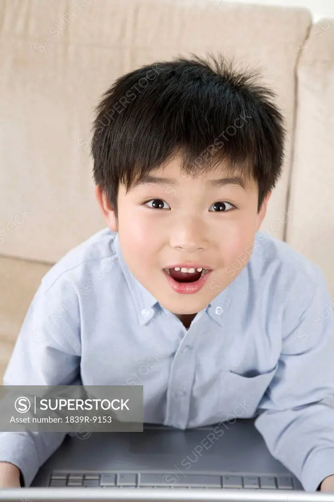 Excited boy looks at camera while using laptop