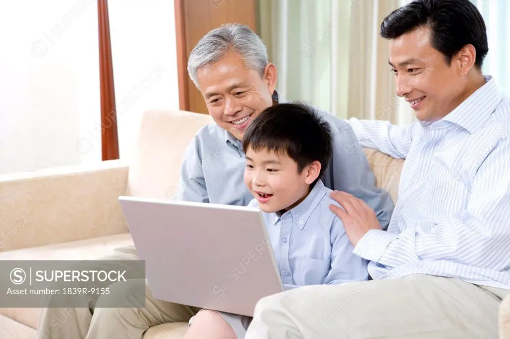Grandfather, father, and son use laptop on a sofa