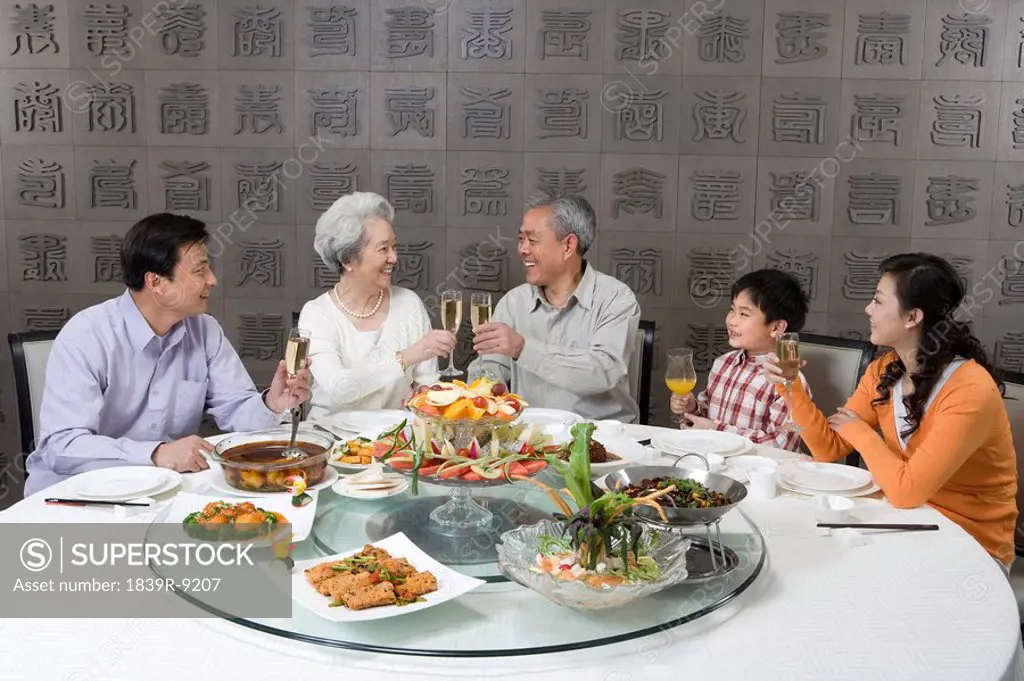 Parents and grandparents with son toasting at dinner table