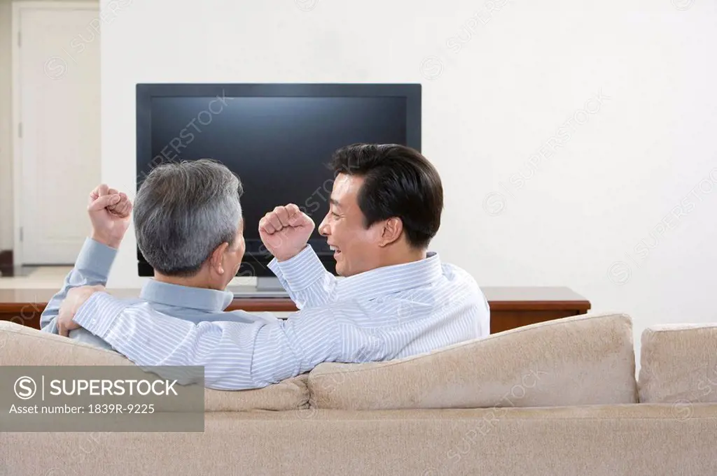 Father and adult son playing rock, scissors, paper in front of widescreen television