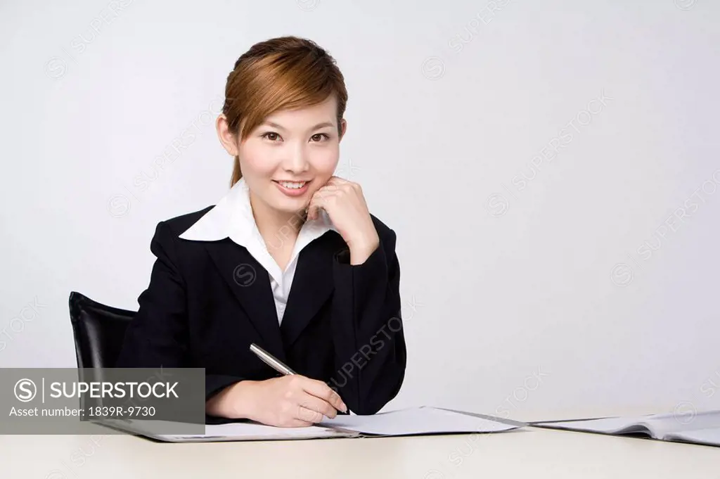 Young businesswoman smiling at camera, pen in hand