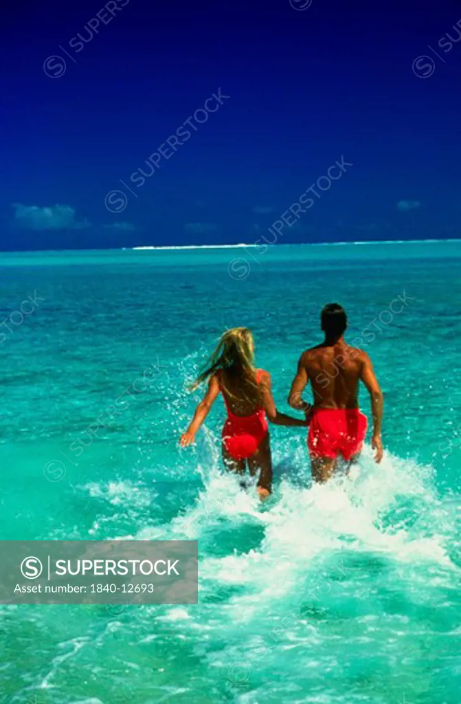 Couple running into the lagoon on the island of Bora Bora, Society Islands, French Polynesia, South Pacific.