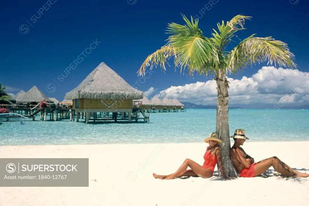Couple under palm tree at Moana Beach Park Royal Hotel on island of Bora Bora, Society Islands, French Polynesia.