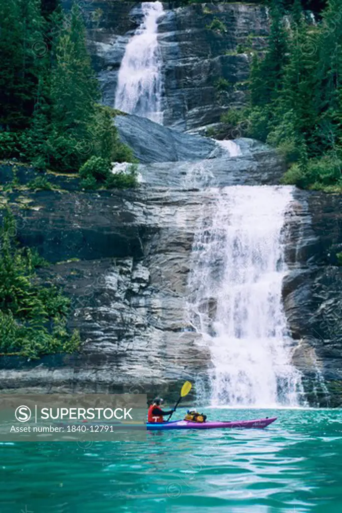 Kayaking below a waterfall along Endicott Arm Fiord in Southeast Alaska in the Tracy Arm Wilderness. Tongass National Forest.