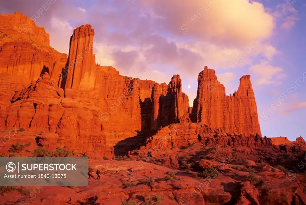 Two hikers approaching the Fisher Towers as the sun sets east of Moab, Utah.