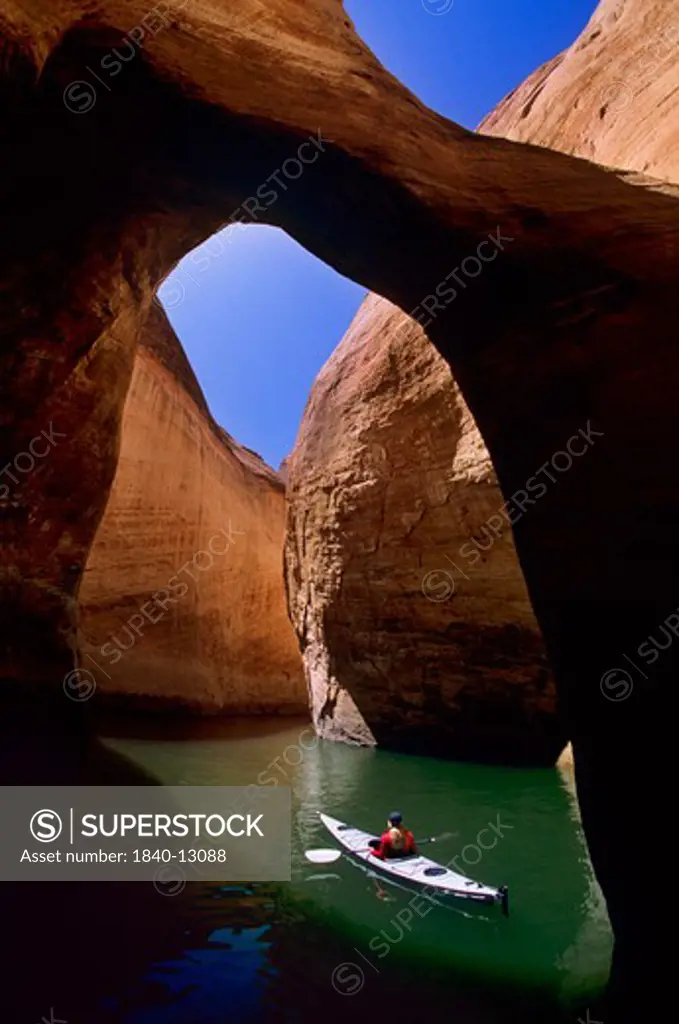 Kayaking on Lake Powell beneath a natural bridge in Anasazi Canyon with water level of the reservoir 110 feet below its ""normal"" full-pool elevation due to a prolonged western drought. At this water level, the reservoir's water volume is 45% of its full-pool capacity. The reservoir's high-water mark, as indicated by the ""bathtub ring"", can be seen at the very top of the canyon wall at center left. Glen Canyon National Recreation Area, Utah. Photo Date: April 2006