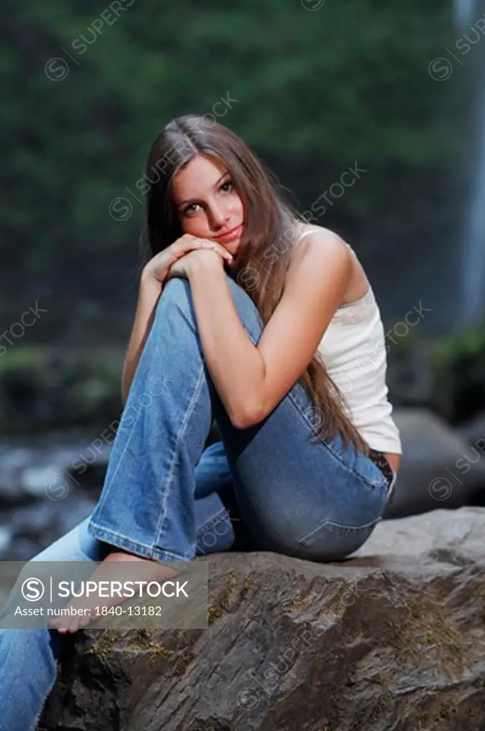 barefoot teenage girl sitting on a rock while looking at the viewer