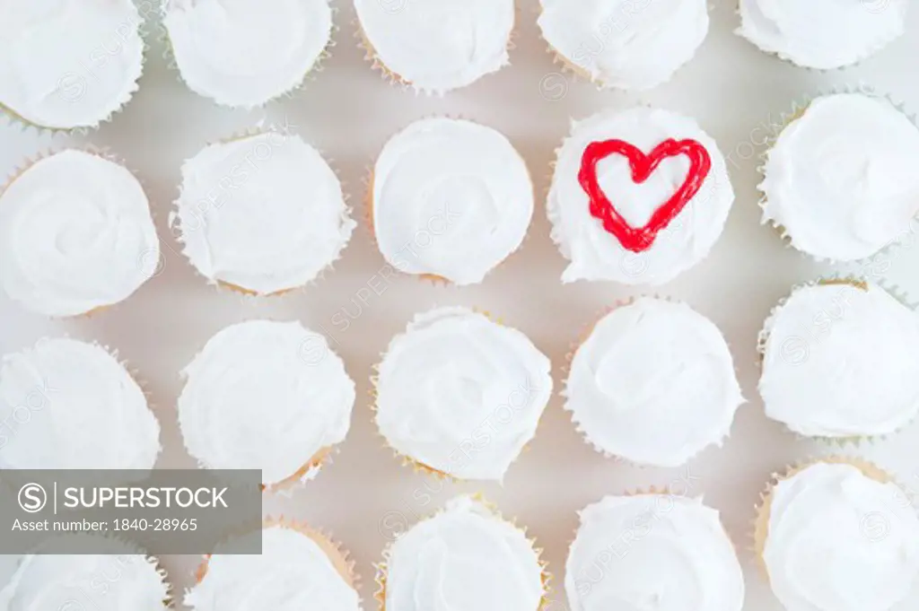 White frosted cupcakes in a row with heart shape on one of the cupcakes