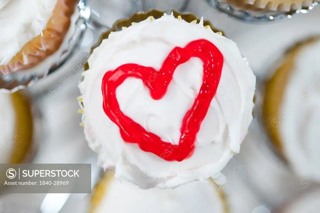 Cupcakes in holder with a red heart drawn on top of white frosting