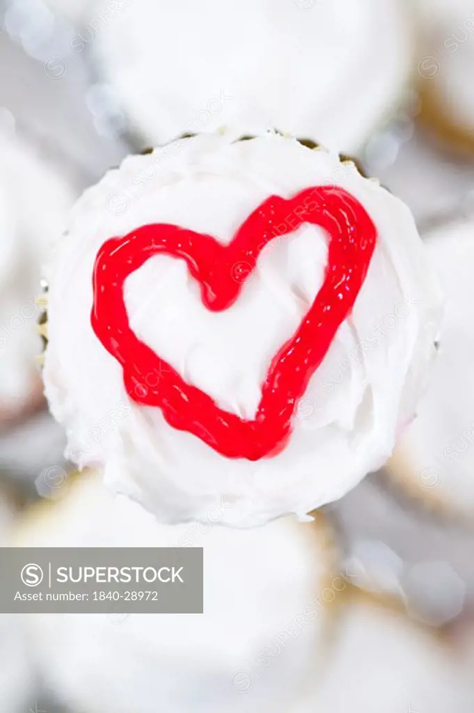 Cupcakes in holder with a red heart drawn on top of white frosting