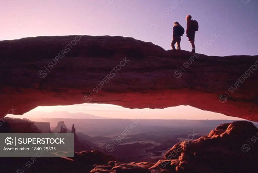 Copyright James Kay.  Two hikers watch the sunrise from atop Mesa Arch in the Island in the Sky district of Canyonlands National Park in southern Utah.  We have extensive files on all the national parks and other ares in southern Utah and the Colorado Plateau.